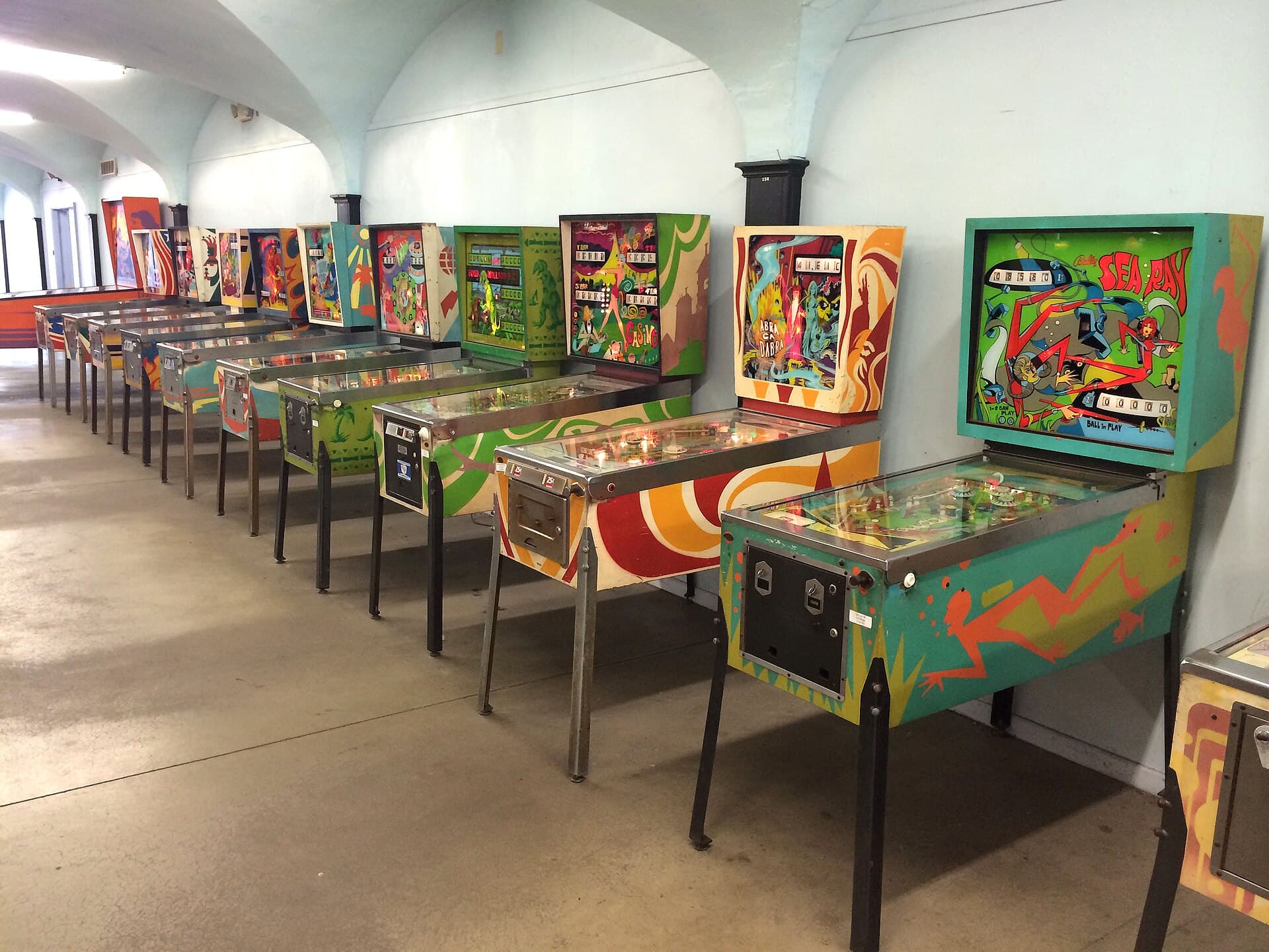 A long row of 1970s pinball machines under a vaulted ceiling
